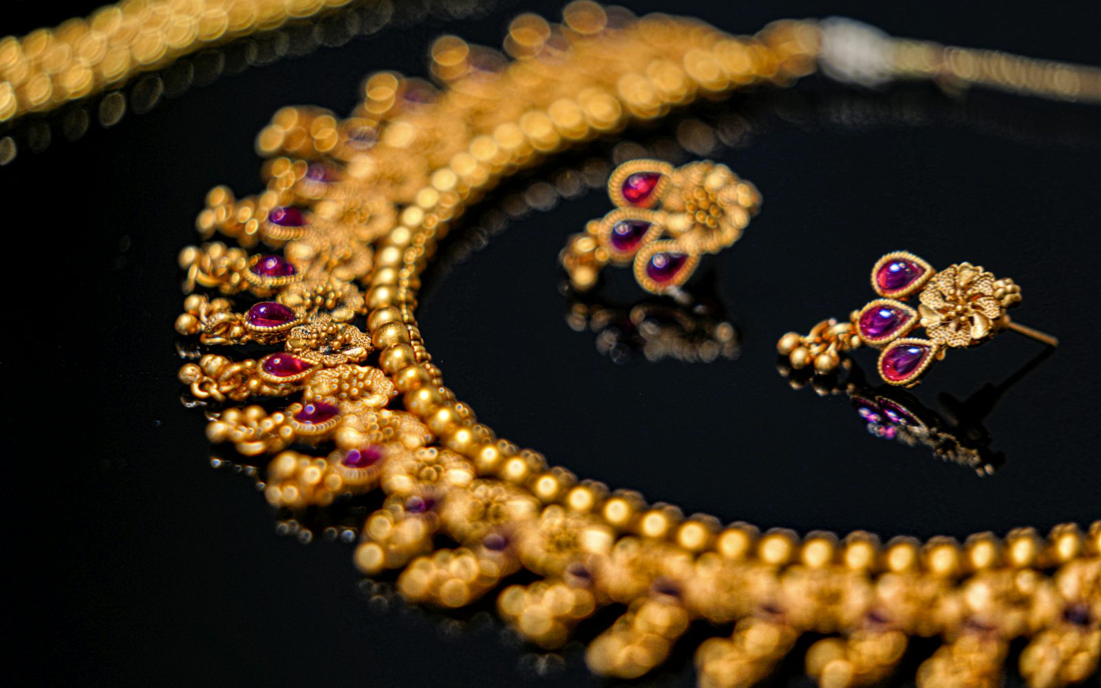 Gold-finish necklace with purple stones and matching earrings on a dark background